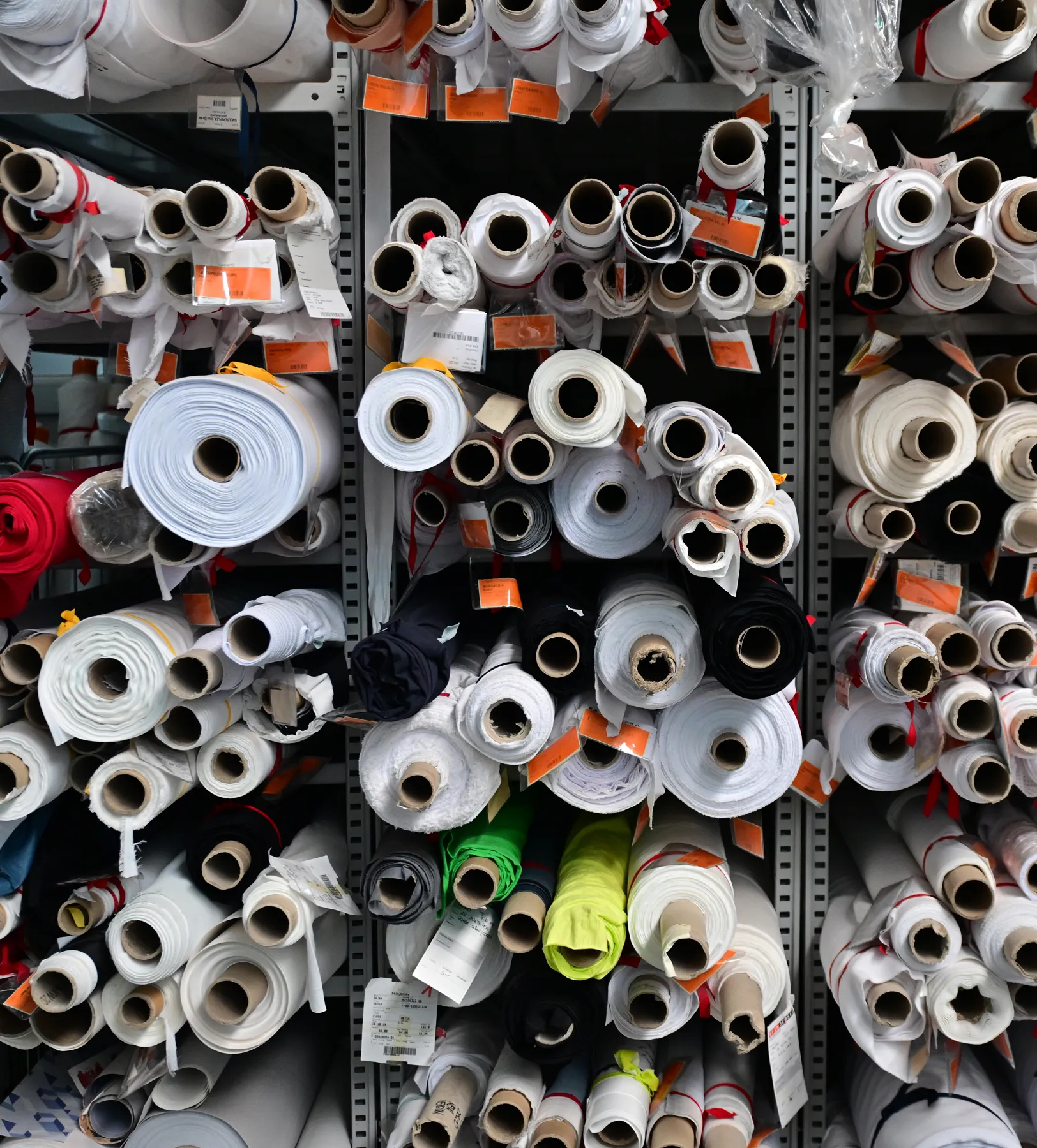 Shelves filled with various rolls of fabric in different colors and sizes, stored for the production of customized sportswear.