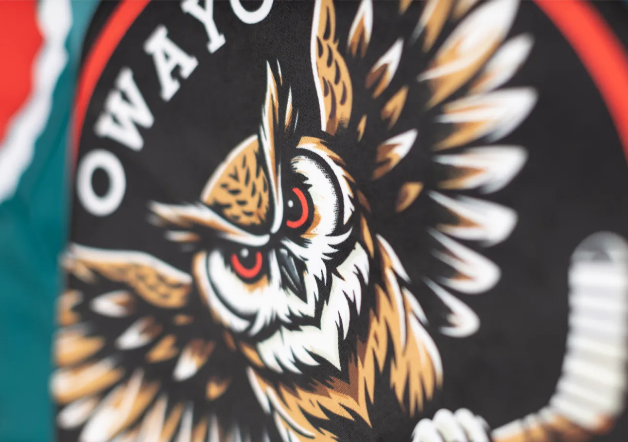 A stylized owl head with red eyes on a black background, surrounded by a red and white circle, on a piece of sportswear from owayo.