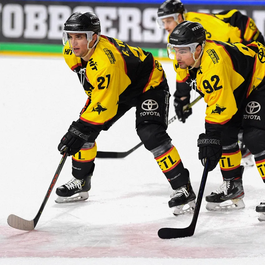Two ice hockey players in yellow and black jerseys are standing on the ice, preparing for the game.