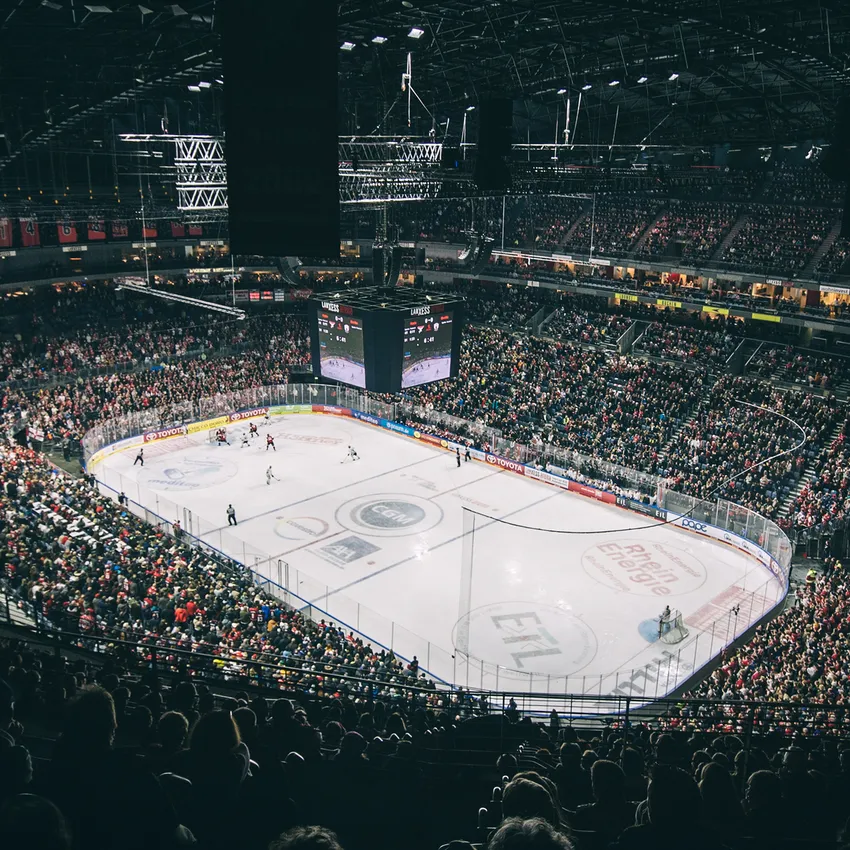 A packed ice hockey arena during a game, featuring players on the ice and a large scoreboard in the background.
