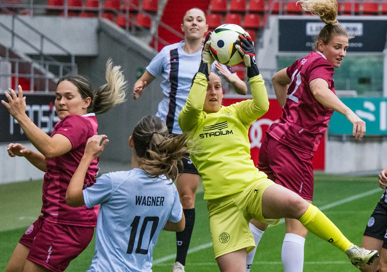 A goalkeeper in yellow sportswear catches a soccer ball while other players in different jerseys compete for possession.