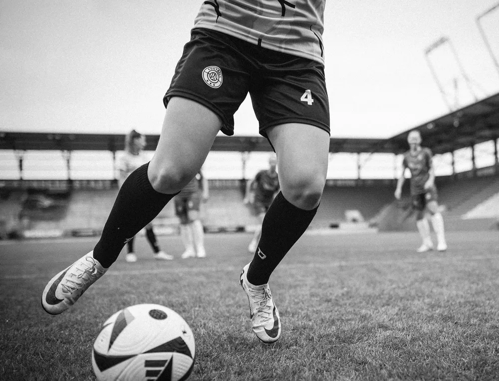 A female soccer player in shorts and long socks playing with a ball on the field.