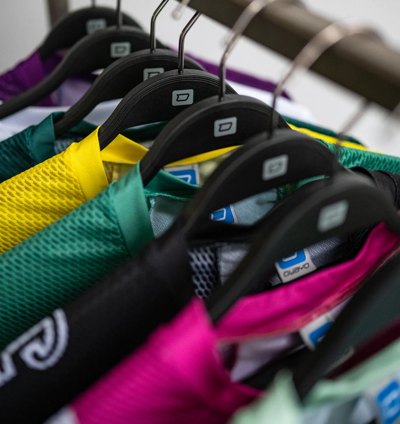 Several colorful, customized sportswear items hang on black hangers.