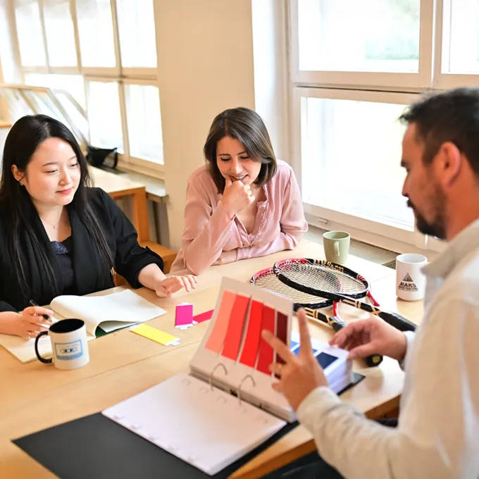 Three people sit at a table discussing color palettes and designs for customized sportswear.
