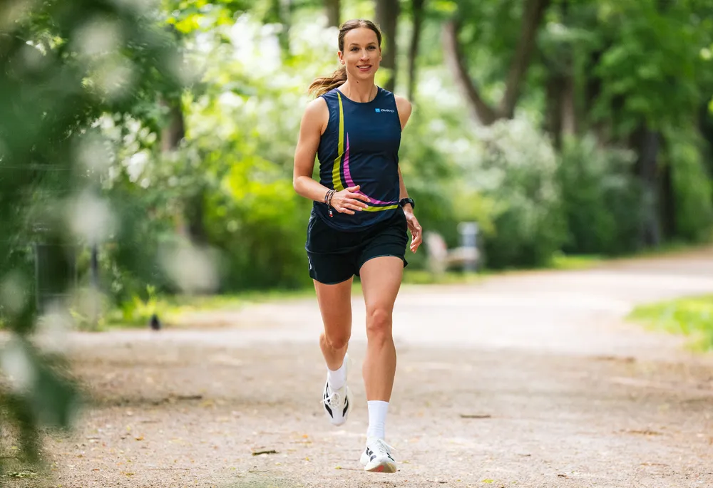 A sporty woman is running on a path outdoors, wearing a blue sports tank top with colorful accents and shorts.