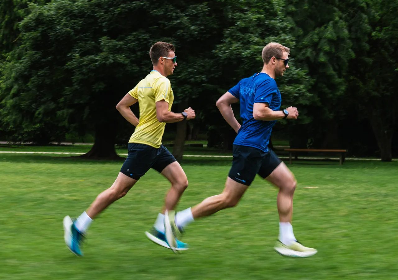 Two runners in sportswear are running across a green field.