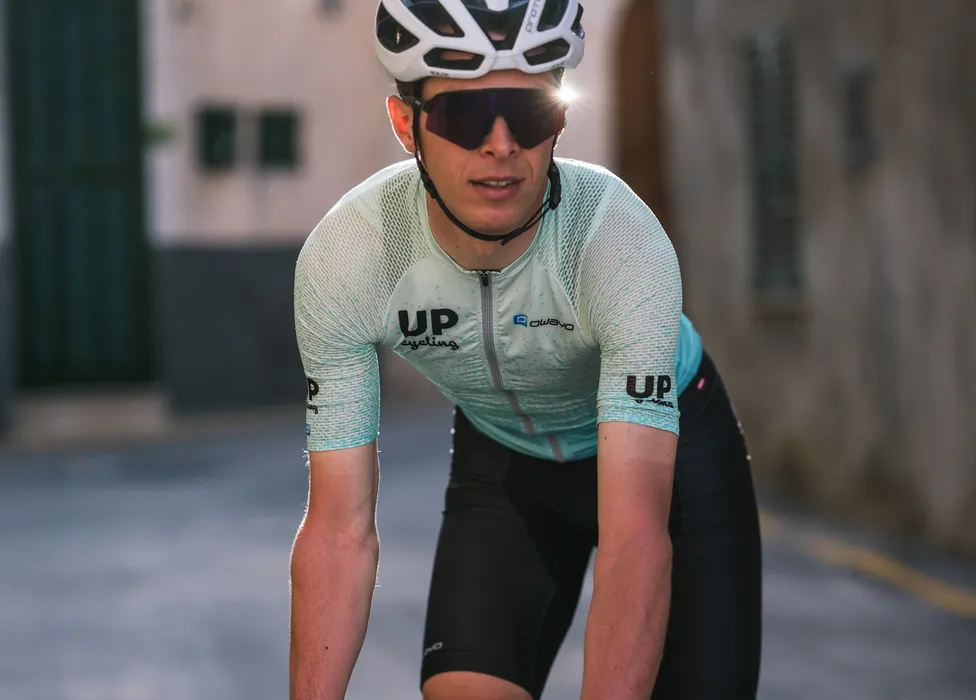 A cyclist wearing a light blue, breathable cycling jersey with the 'UP cycling' and 'owayo' logos on the chest, in a sporty posture on a street.