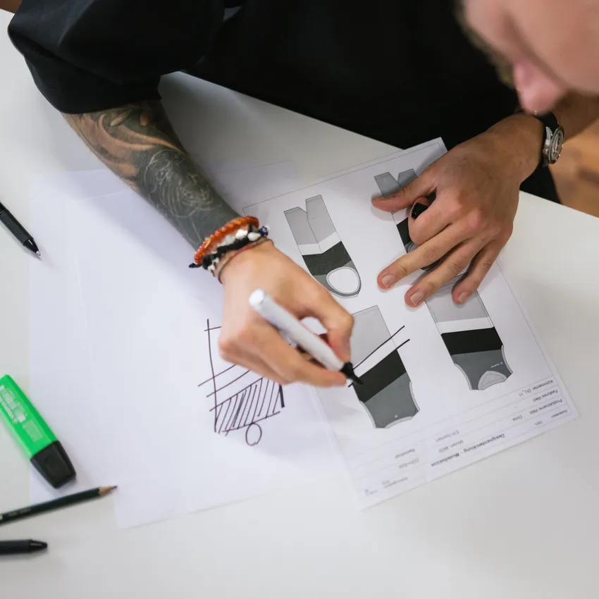 A person sketches designs for sportswear on paper, surrounded by pens and markers.