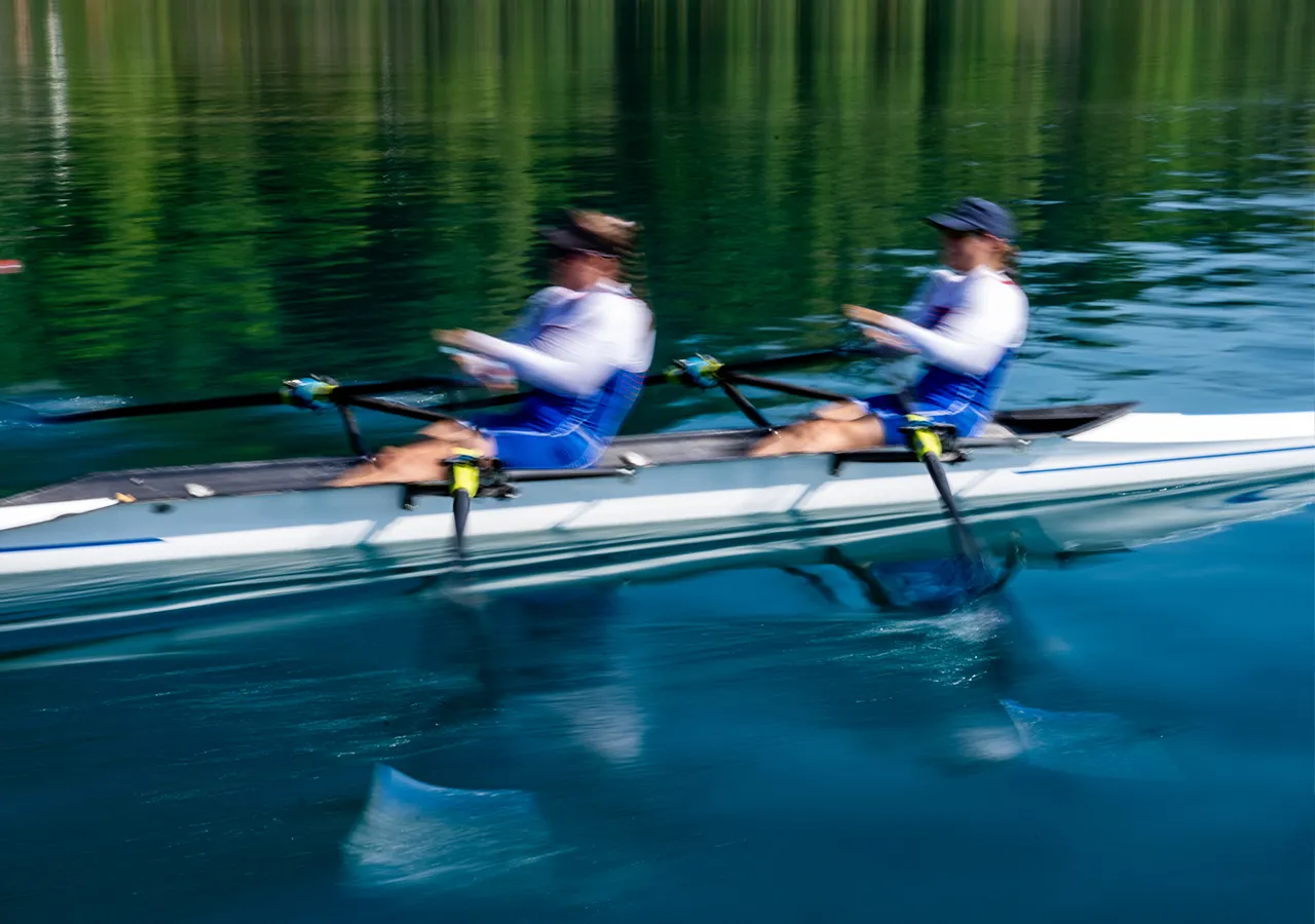 Two rowers in blue sportswear are rowing in sync on a calm water surface.