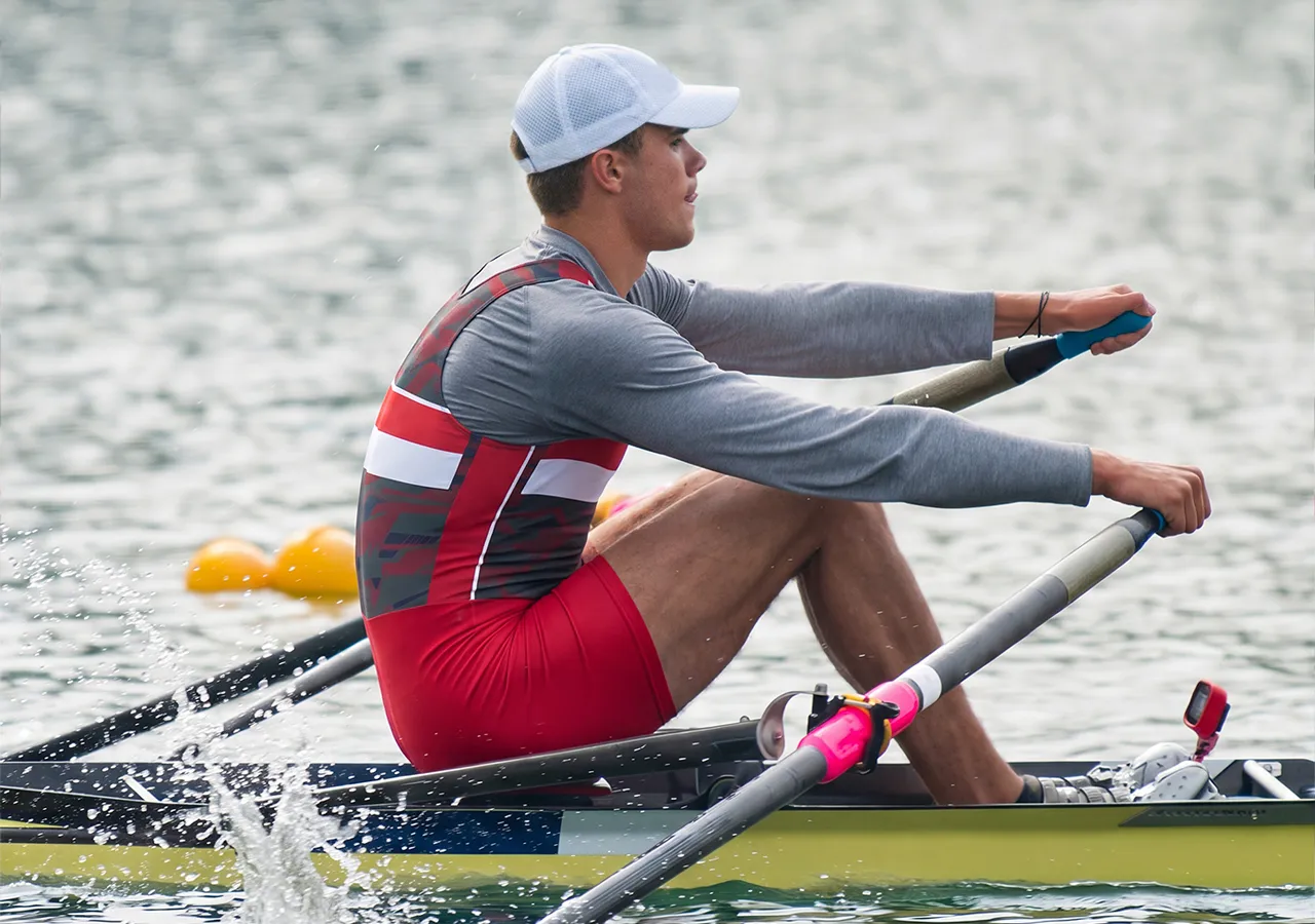 A rower in a red and gray sports outfit is rowing on a body of water.